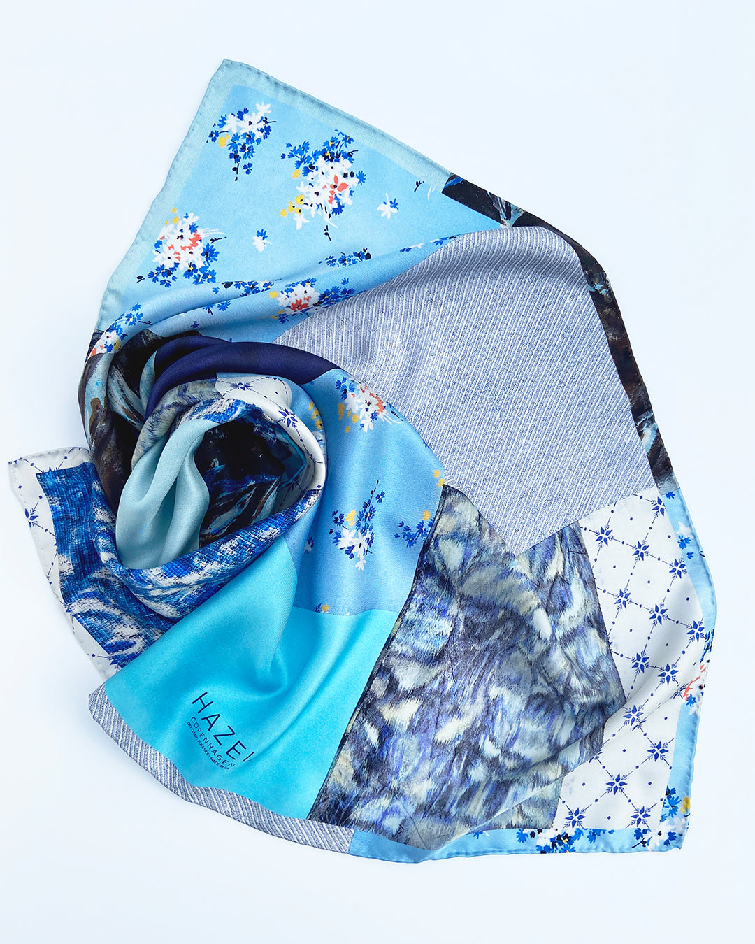 Kvadratisk silketørklæde med blå blomster, silketørklæde i lys blå, silketørklæde med patchworkmønster, Silketørklæde blå farver, Silketørklæde lys blå, silketørklæde multifarvet blåt. silketørklæde med mørk blå farve,  Silketørklæde kvadratisk 65 x 65 cm, Silketørklæde i 100 % ren silke, silketørklæde i ægte silke twill, silketørklæde med design af Susanne Schjerning, silketørklæde med rullede kanter. Giv et silketørklæde i gave. Bæredygtigt silketørklæde i dansk design.