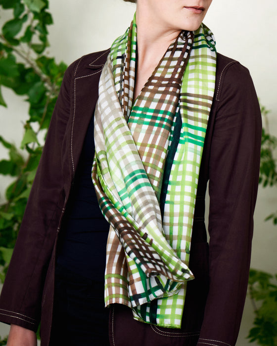 Aflangt silketørklæde i grønne farver, silketørklæde i brune farver, Silketørklæde lyst ternet, Silketørklæde med grønne og brune håndmalede tern, Silketørklæde aflangt 160 x 65 cm, Silketørklæde i 100 % ren silke, silketørklæde i ægte silke twill, silketørklæde med design af Susanne Schjerning, silketørklæde med rullede kanter. Giv et silketørklæde i gave. Bæredygtigt silketørklæde i bæredygtig dansk design, silketørklædet der er nemt at binde. 