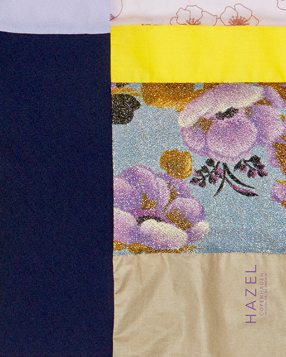 Kvadratisk silketørklæde med lilla blomster, silketørklæde i lys lilla, silketørklæde med patchworkmønster, Silketørklæde lilla farve, Silketørklæde gult, silketørklæde multifarvet. silketørklæde med sort farve,  Silketørklæde kvadratisk 65 x 65 cm, Silketørklæde i 100 % ren silke, silketørklæde i ægte silke twill, silketørklæde med design af Susanne Schjerning, silketørklæde med rullede kanter. Giv et silketørklæde i gave. Bæredygtigt silketørklæde i dansk design.
