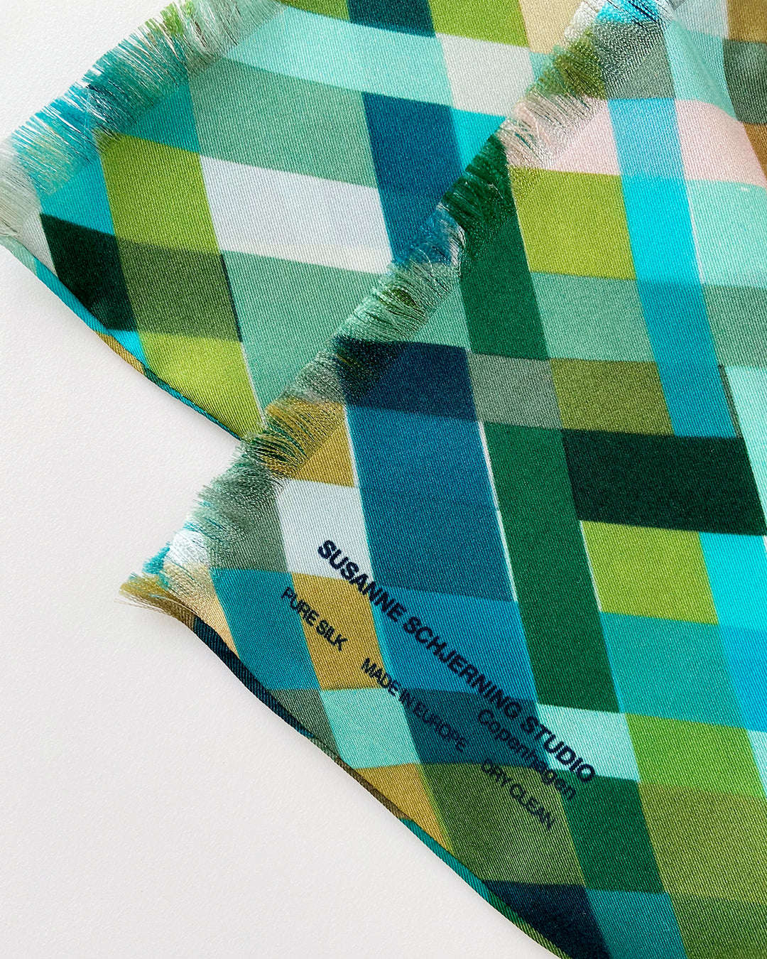 Aflangt silketørklæde med harlekintern, grønt silketørklæde, Silketørklæde i turkis farve, Silketørklæde i blå farve, silketørklæde i grøn farve, silketørklæde i multifarvede grønne harlekintern tern,  Silketørklæde aflangt 180 x 65 cm, Silketørklæde i 100 % ren silke, silketørklæde i ægte silke twill, silketørklæde med design af Susanne Schjerning, silketørklæde med rullede kanter. Giv et silketørklæde i gave. Bæredygtigt silketørklæde i dansk design.